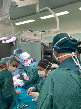The theatre team working beneath a large multi-head surgical lamp, with the anaesthetic machine and patient monitor behind them.