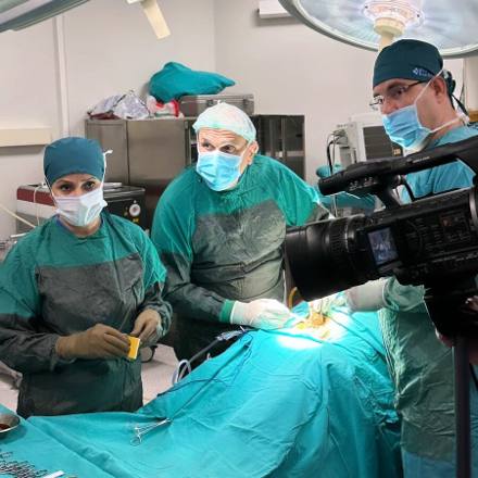 A video camera trained on the operating table while the scrubbed team continues the procedure, part of the clinic’s teaching record.