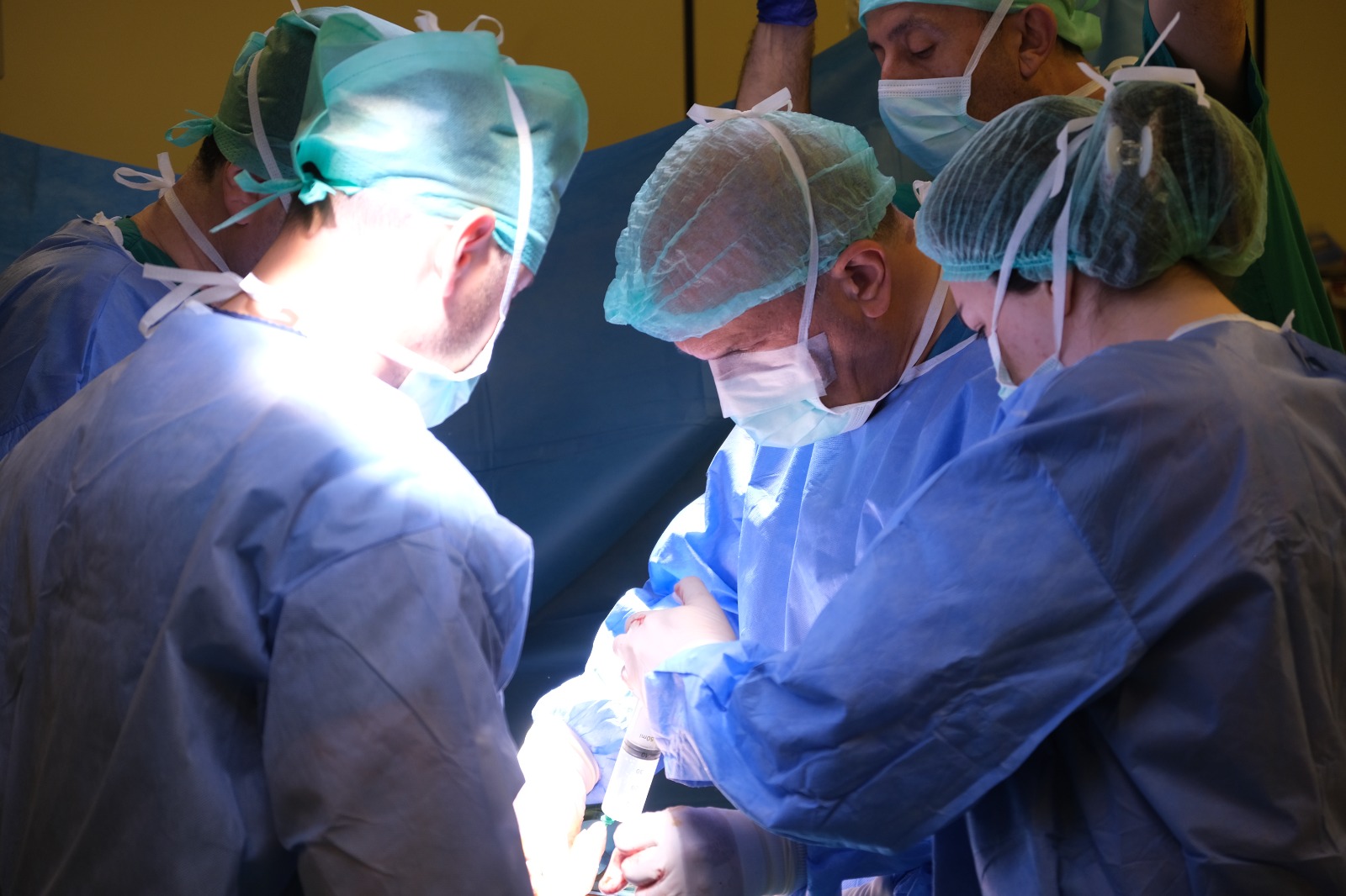 The surgical team working together around the operating table under theatre lights.
